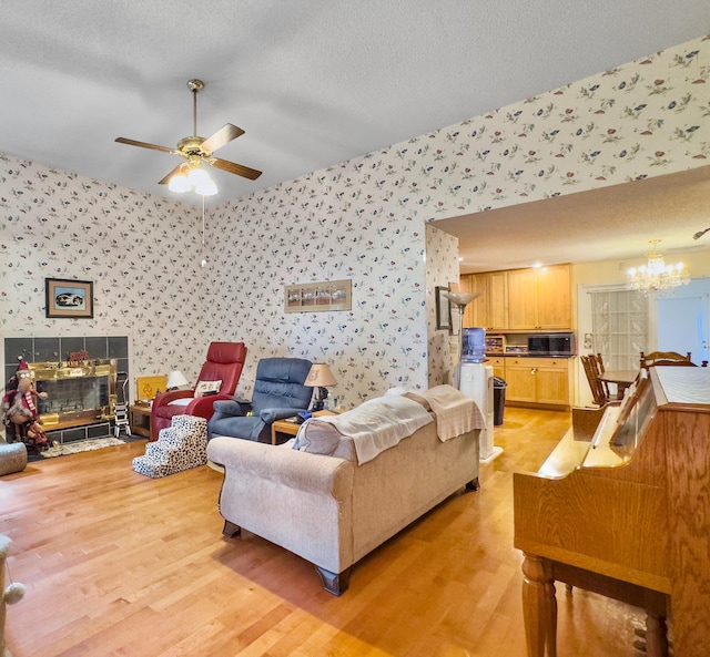 living room featuring ceiling fan with notable chandelier, light hardwood / wood-style floors, and a textured ceiling