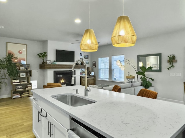 kitchen with sink, hanging light fixtures, light stone countertops, white cabinets, and stainless steel dishwasher