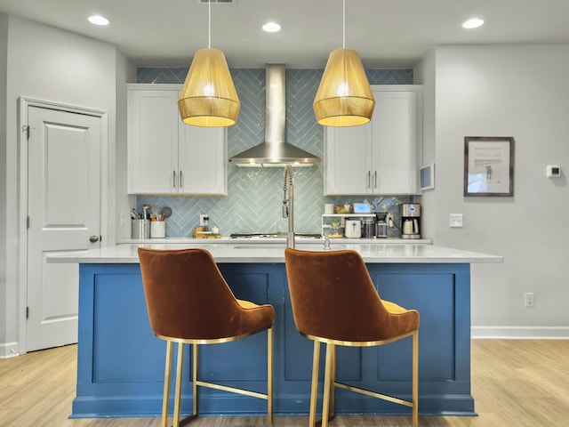 kitchen featuring white cabinetry, wall chimney range hood, hanging light fixtures, and a kitchen bar