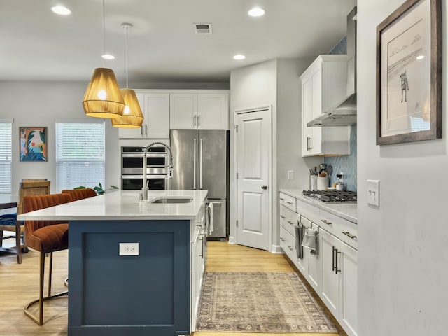 kitchen with white cabinetry, decorative light fixtures, a kitchen island with sink, and wall chimney range hood