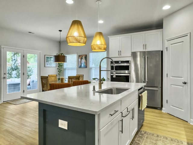 kitchen featuring white cabinetry, hanging light fixtures, stainless steel appliances, light stone counters, and an island with sink