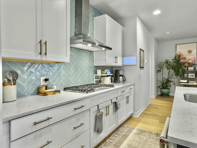 kitchen featuring white cabinetry, stainless steel gas stovetop, light stone countertops, and wall chimney range hood