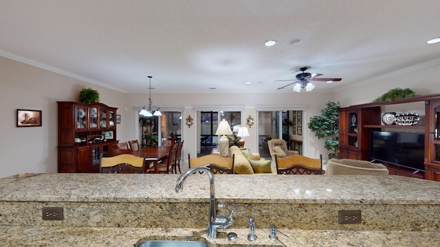 kitchen featuring crown molding, ceiling fan, light stone countertops, pendant lighting, and open floor plan