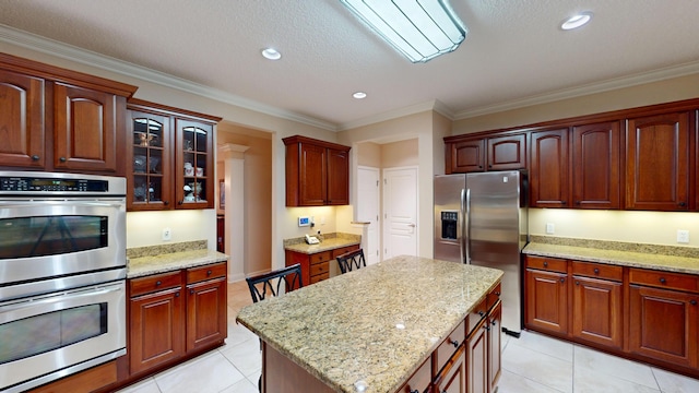 kitchen with appliances with stainless steel finishes, light tile patterned floors, glass insert cabinets, light stone countertops, and ornamental molding