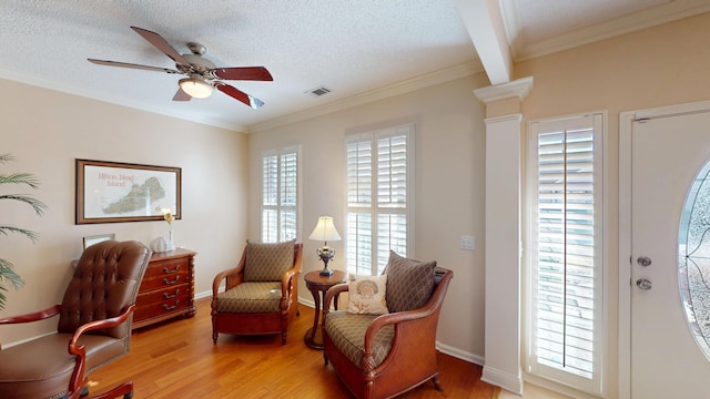 living area featuring light wood-type flooring, a ceiling fan, ornamental molding, a textured ceiling, and decorative columns