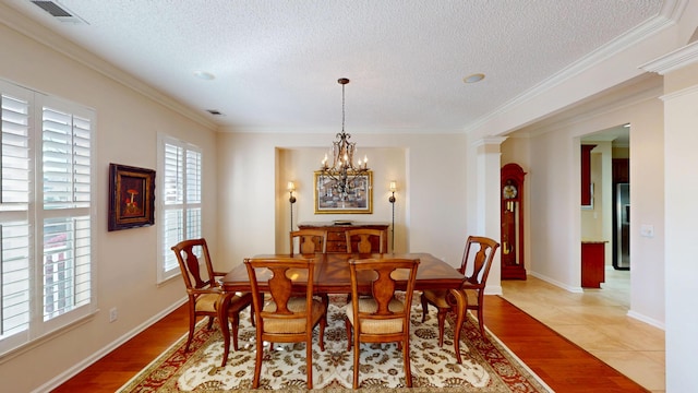 dining space with a textured ceiling, a chandelier, wood finished floors, ornamental molding, and decorative columns