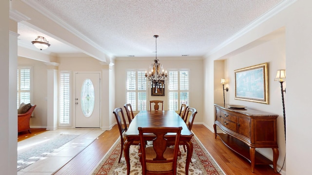dining area with light wood-style flooring, a textured ceiling, a chandelier, ornamental molding, and decorative columns