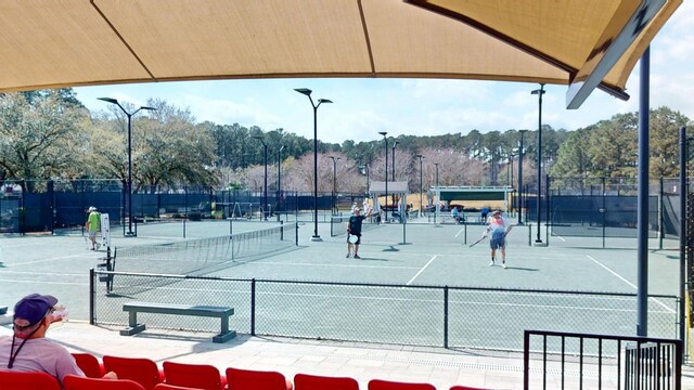 view of tennis court featuring view of wooded area