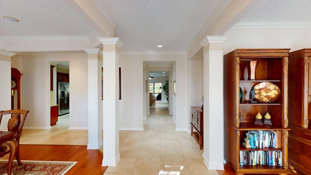 corridor featuring ornate columns, a textured ceiling, crown molding, and light wood-style floors