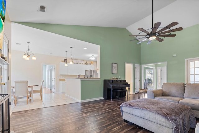 living area with high vaulted ceiling, ceiling fan with notable chandelier, wood finished floors, visible vents, and baseboards