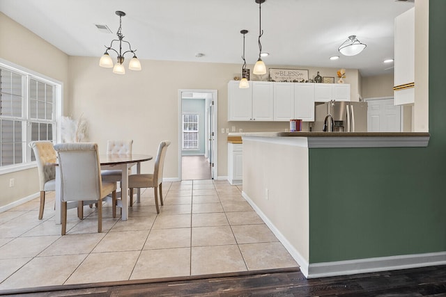 kitchen with light tile patterned floors, visible vents, white cabinets, stainless steel fridge with ice dispenser, and hanging light fixtures