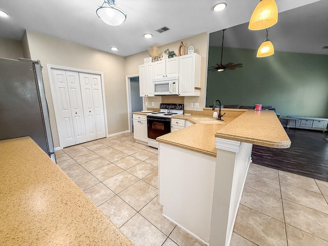 kitchen featuring electric stove, white microwave, freestanding refrigerator, a sink, and a peninsula