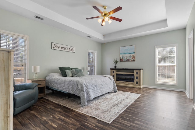 bedroom with dark wood finished floors, a raised ceiling, visible vents, and baseboards