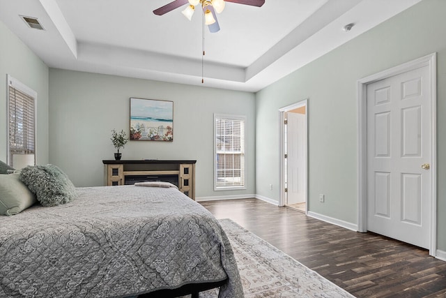 bedroom with ceiling fan, dark wood-style flooring, visible vents, baseboards, and a raised ceiling