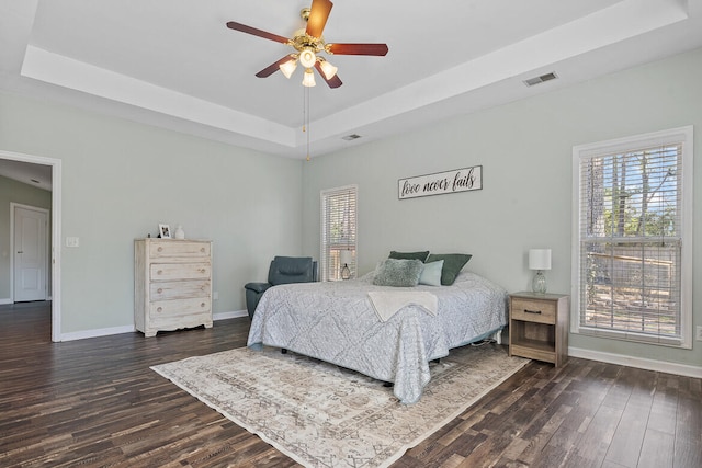 bedroom featuring baseboards, visible vents, a raised ceiling, dark wood-style flooring, and multiple windows