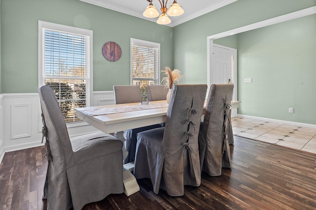 dining space with crown molding, a chandelier, wood finished floors, and wainscoting