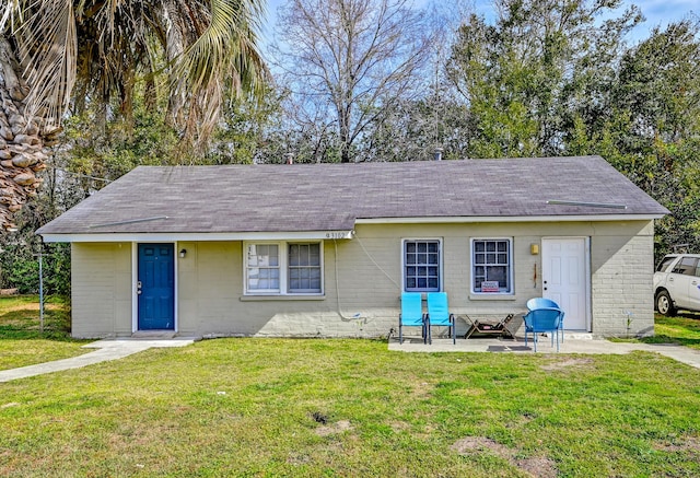 view of front of home with a shingled roof, a front yard, and concrete block siding