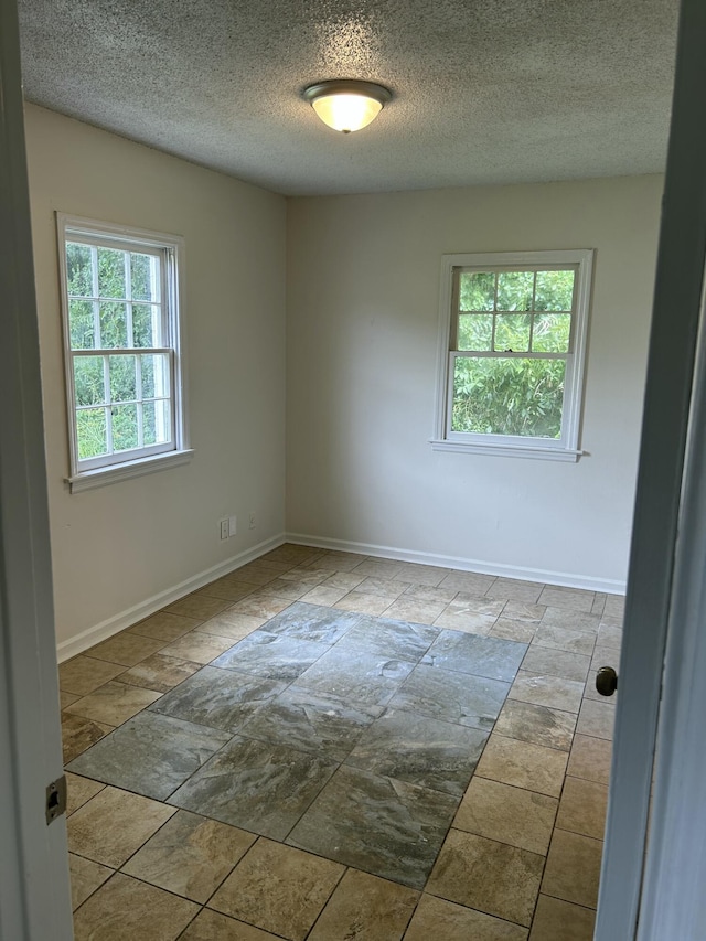 empty room with a textured ceiling, baseboards, and stone finish floor