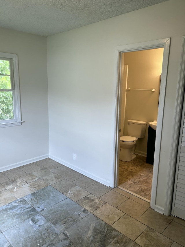 unfurnished bedroom with a textured ceiling, connected bathroom, and baseboards