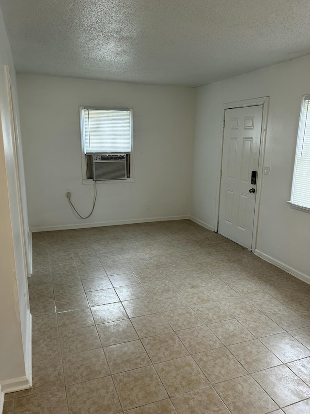 unfurnished room featuring cooling unit, a textured ceiling, baseboards, and light tile patterned floors