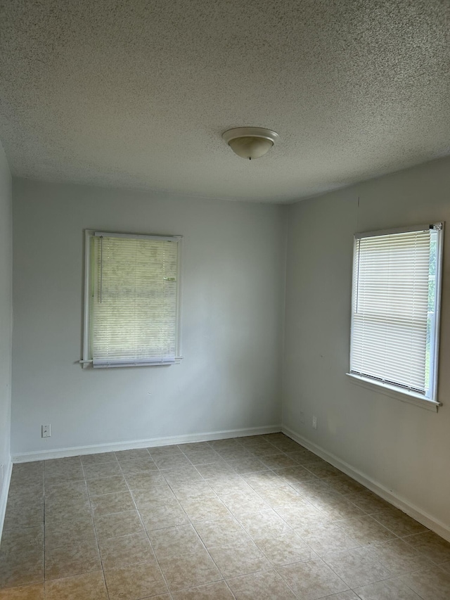 unfurnished room featuring a textured ceiling, tile patterned flooring, and baseboards