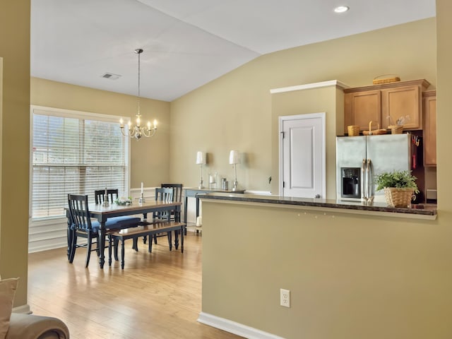 kitchen with dark stone counters, an inviting chandelier, stainless steel fridge with ice dispenser, light hardwood / wood-style floors, and hanging light fixtures