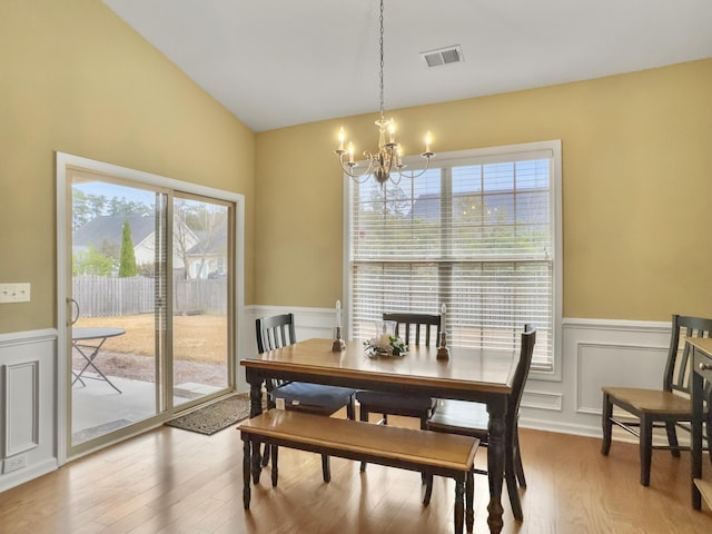 dining room with hardwood / wood-style flooring, vaulted ceiling, a wealth of natural light, and a chandelier