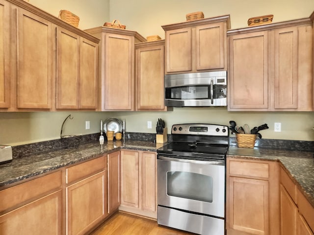 kitchen featuring appliances with stainless steel finishes, light hardwood / wood-style floors, and dark stone countertops