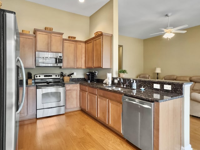 kitchen with kitchen peninsula, stainless steel appliances, sink, dark stone countertops, and light hardwood / wood-style floors