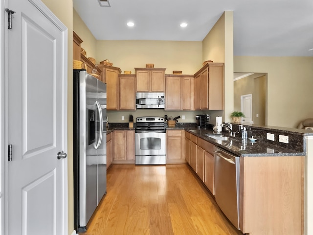 kitchen with sink, stainless steel appliances, light hardwood / wood-style flooring, kitchen peninsula, and dark stone countertops