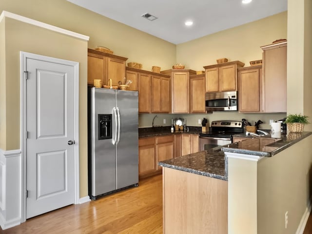 kitchen featuring kitchen peninsula, appliances with stainless steel finishes, light hardwood / wood-style floors, and dark stone counters