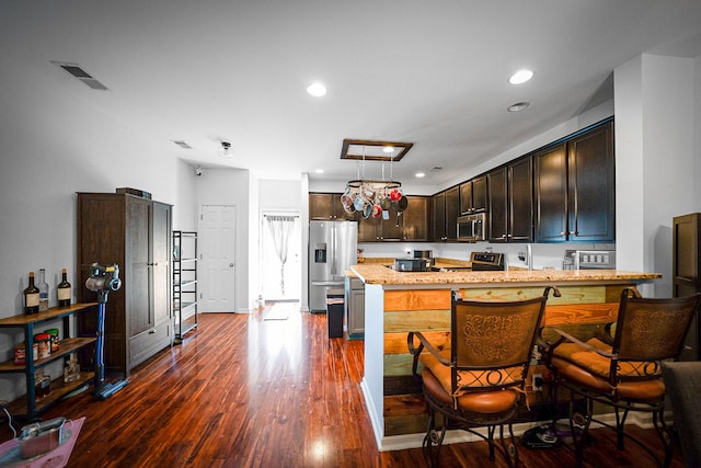 kitchen featuring a breakfast bar, light stone countertops, stainless steel appliances, and dark hardwood / wood-style floors