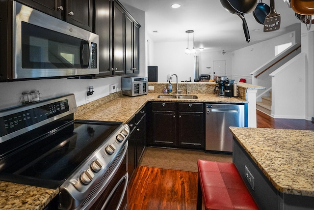 kitchen featuring dark hardwood / wood-style floors, hanging light fixtures, stainless steel appliances, kitchen peninsula, and sink