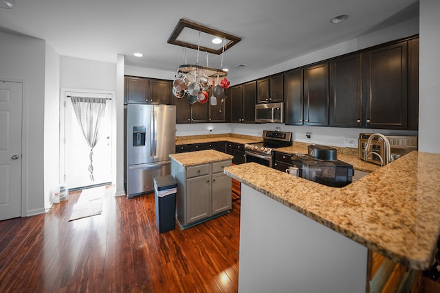 kitchen with dark brown cabinets, light stone counters, a kitchen island, dark hardwood / wood-style floors, and stainless steel appliances