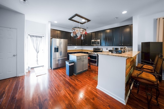 kitchen with light stone countertops, appliances with stainless steel finishes, dark hardwood / wood-style flooring, a center island, and pendant lighting