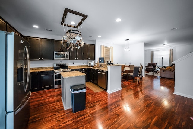 kitchen featuring light stone countertops, appliances with stainless steel finishes, a kitchen island, pendant lighting, and dark hardwood / wood-style floors