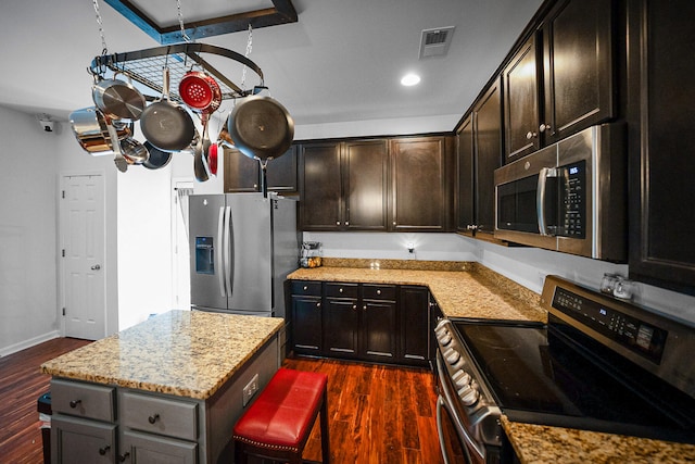 kitchen with light stone countertops, a center island, a kitchen breakfast bar, stainless steel appliances, and dark hardwood / wood-style floors