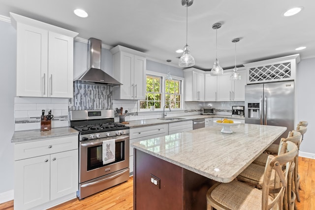 kitchen featuring wall chimney exhaust hood, appliances with stainless steel finishes, a sink, decorative backsplash, and a breakfast bar area