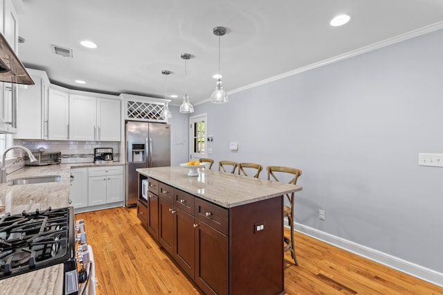 kitchen featuring crown molding, a kitchen bar, visible vents, appliances with stainless steel finishes, and a sink