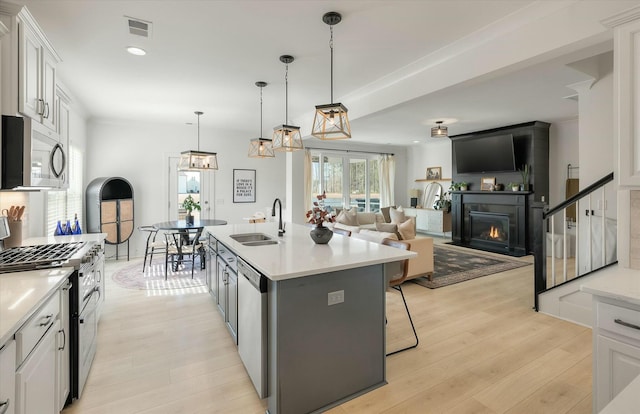 kitchen with decorative light fixtures, sink, white cabinets, stainless steel appliances, and a center island with sink