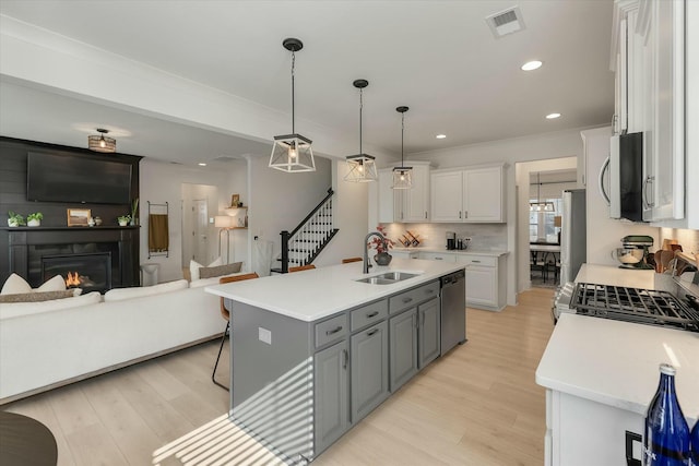 kitchen featuring sink, appliances with stainless steel finishes, white cabinetry, an island with sink, and decorative light fixtures