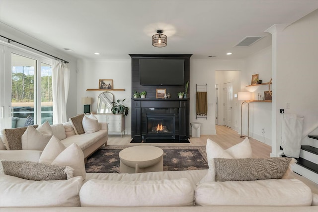 living room featuring ornamental molding, a large fireplace, and light wood-type flooring