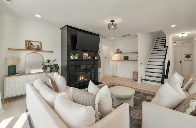 living room featuring crown molding, a large fireplace, and light wood-type flooring