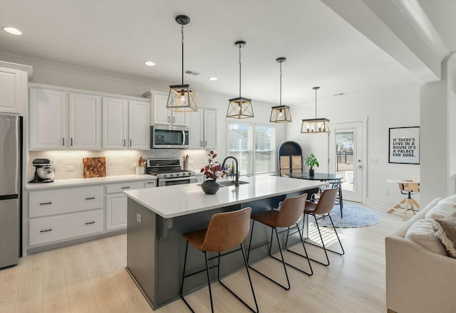 kitchen featuring white cabinetry, appliances with stainless steel finishes, pendant lighting, and a center island with sink