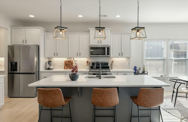 kitchen with white cabinetry, pendant lighting, stainless steel appliances, a kitchen island with sink, and decorative backsplash