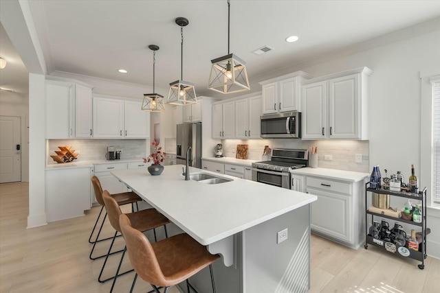 kitchen featuring appliances with stainless steel finishes, decorative light fixtures, white cabinetry, sink, and a center island with sink