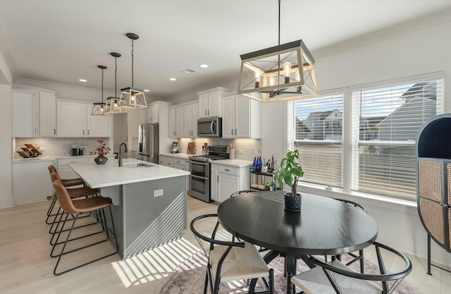 kitchen with sink, hanging light fixtures, appliances with stainless steel finishes, a kitchen island with sink, and white cabinets