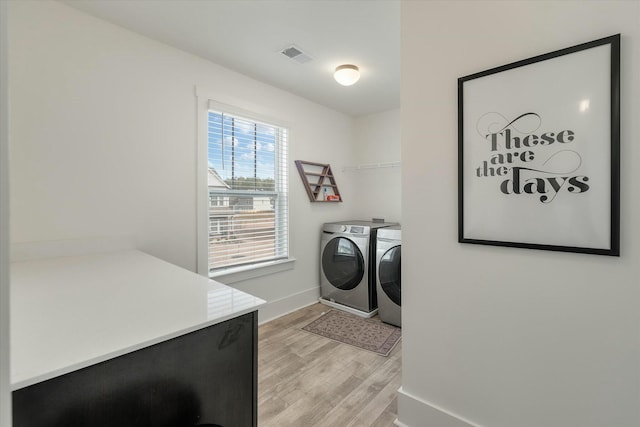 clothes washing area with washing machine and clothes dryer and light hardwood / wood-style flooring