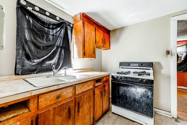 kitchen with brown cabinets, light countertops, white range with gas cooktop, a textured ceiling, and a sink