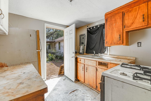 kitchen with light countertops, brown cabinetry, a sink, a textured ceiling, and white gas range oven